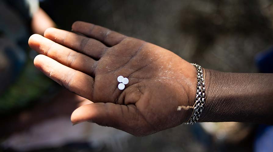 Close-up photo of a hand holding three small white pills.