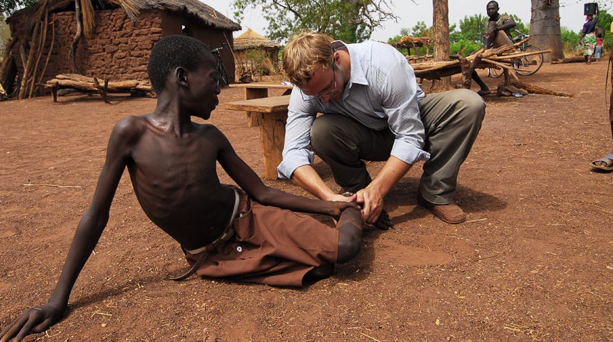 Ten-year-old Fusini Adam winces as Adam Weiss examines the boy’s leg for Guinea worm disease in the village of Nyujaguyili in northern Ghana. Since this photo was taken several years ago, Ghana has eliminated the parasitic disease. (Photo: The Carter Center)