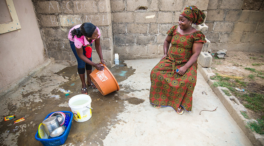 Rahab Joshua sits in her yard while her daughter washes clothes.