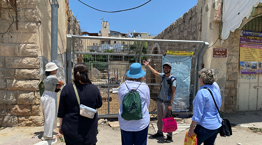 Five people look at what's behind a chain link fence.